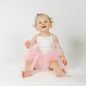 Adorable baby in a pink tutu sitting happily on a white background, radiating joy and innocence.